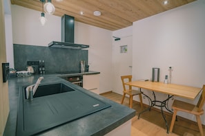 Een moderne keuken met een zwart aanrecht, een roestvrijstalen spoelbak en een houten eettafel met metalen poten.