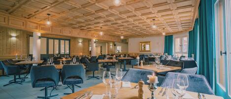 A spacious dining area with multiple tables and chairs, wooden ceiling, and large windows with curtains.