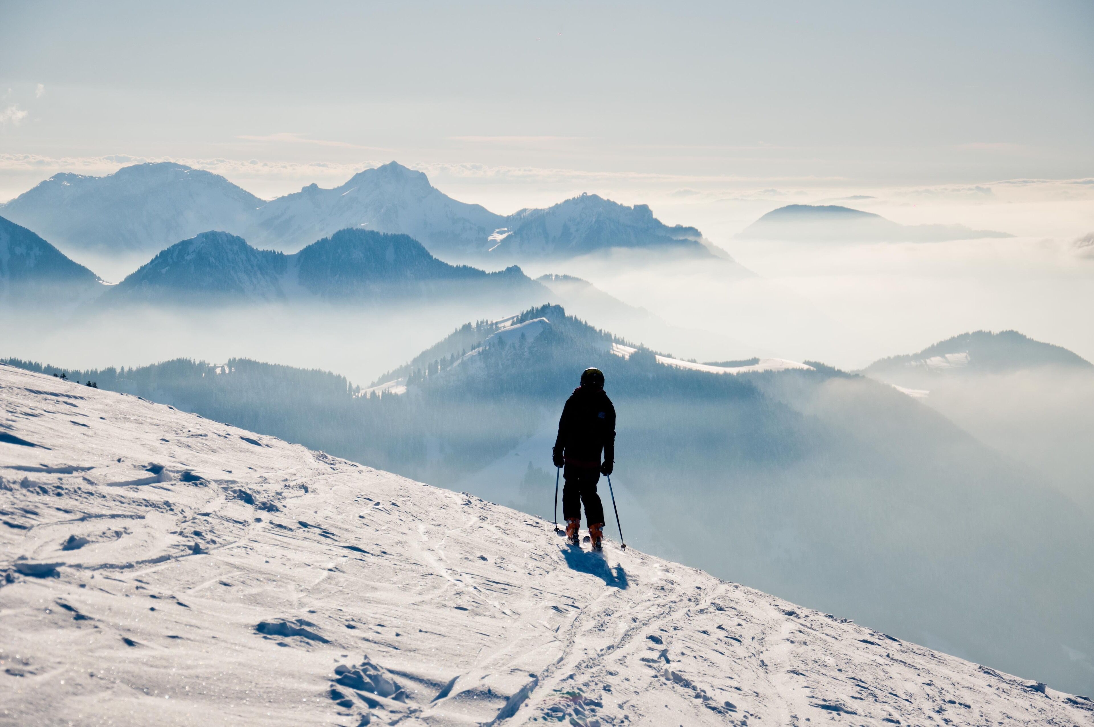 A person skiing on a snowy mountain slope with a view of distant mountains and fog.