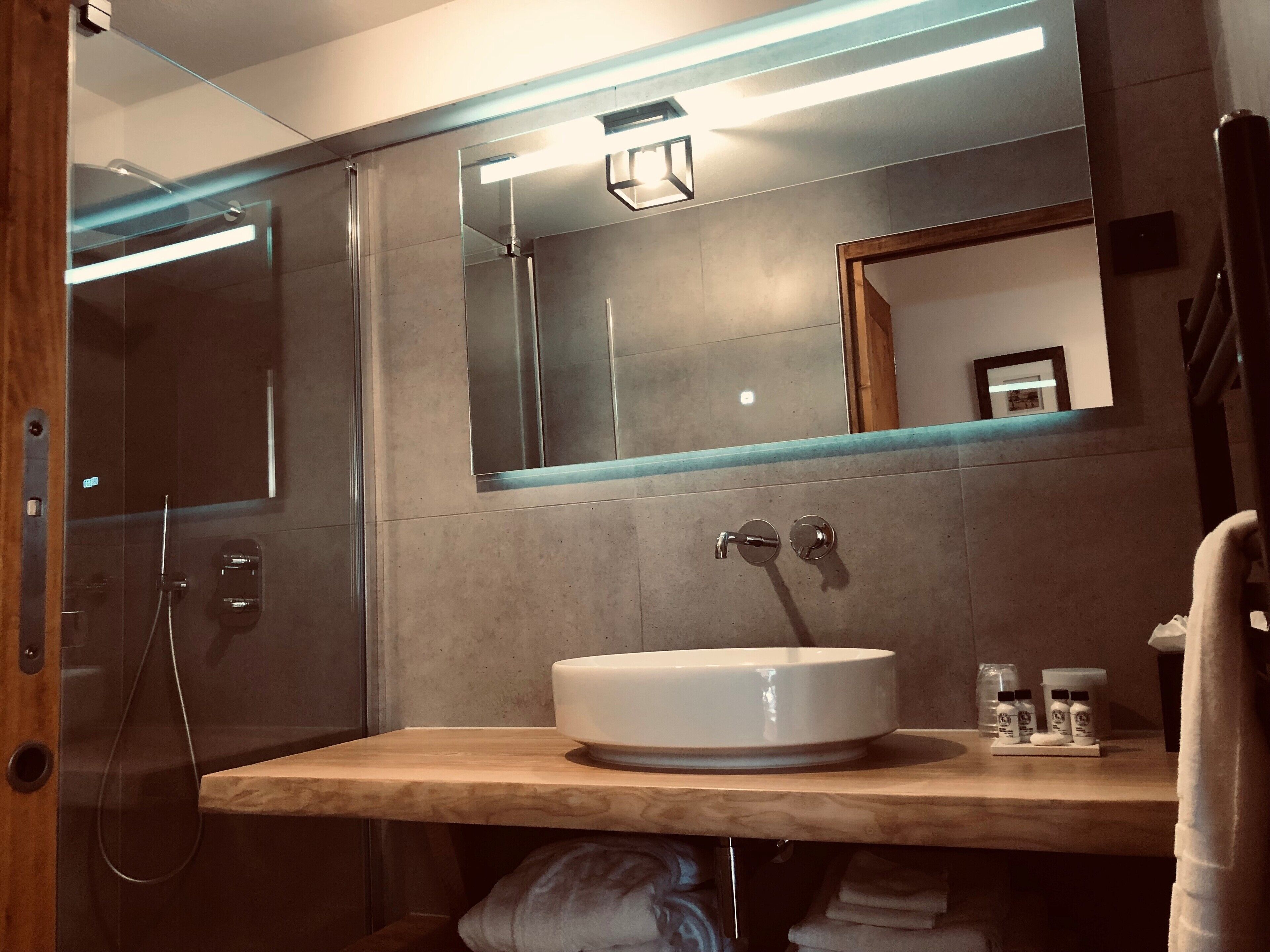 A modern bathroom with a glass-enclosed shower, a large mirror, and a wooden vanity with a sink.