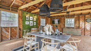 Uma zona de refeições rústica com teto de madeira, parede verde decorada com quadros e uma mesa de bar com cadeiras.