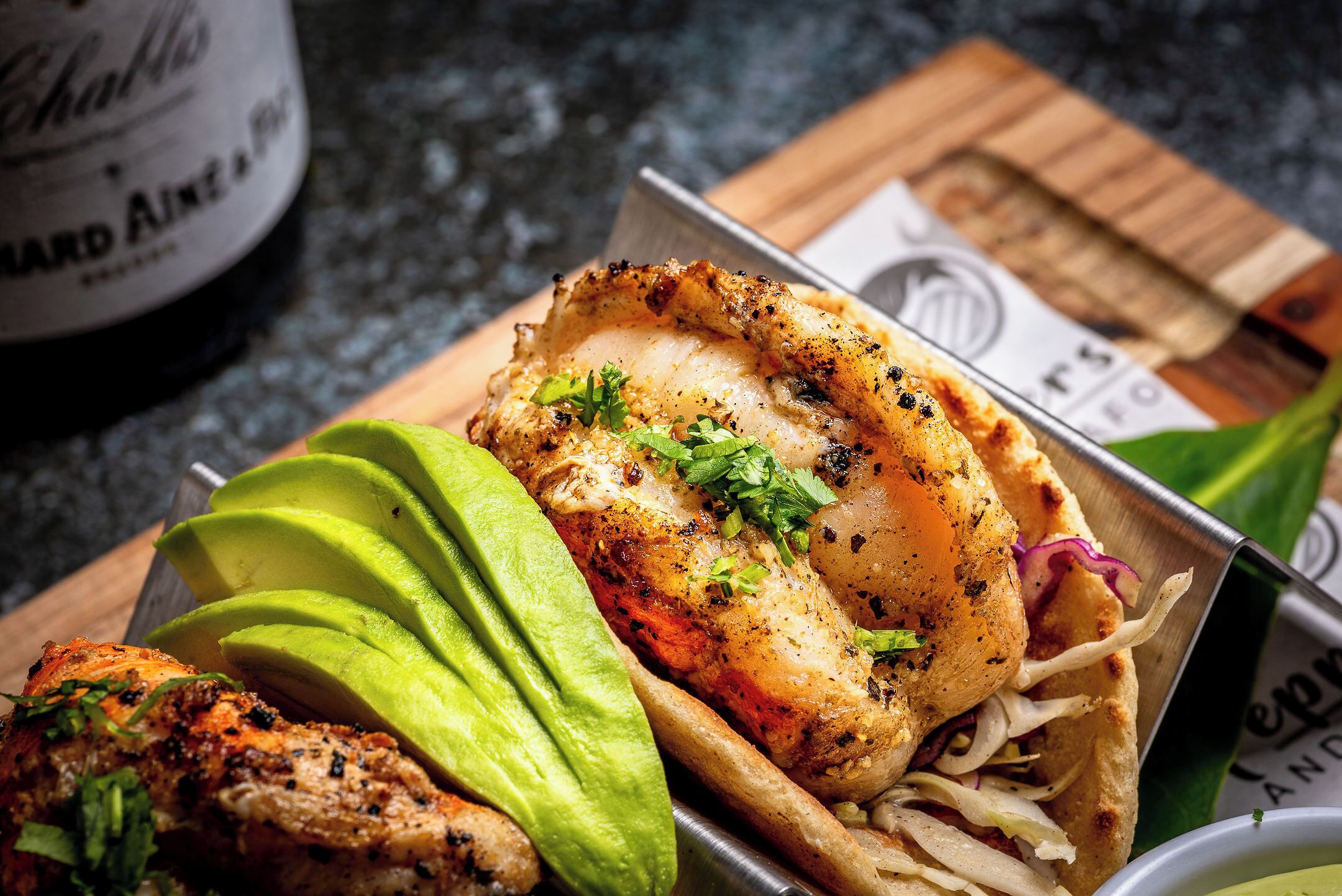 A meal with grilled chicken, avocado slices, and a side of coleslaw in a metal container.