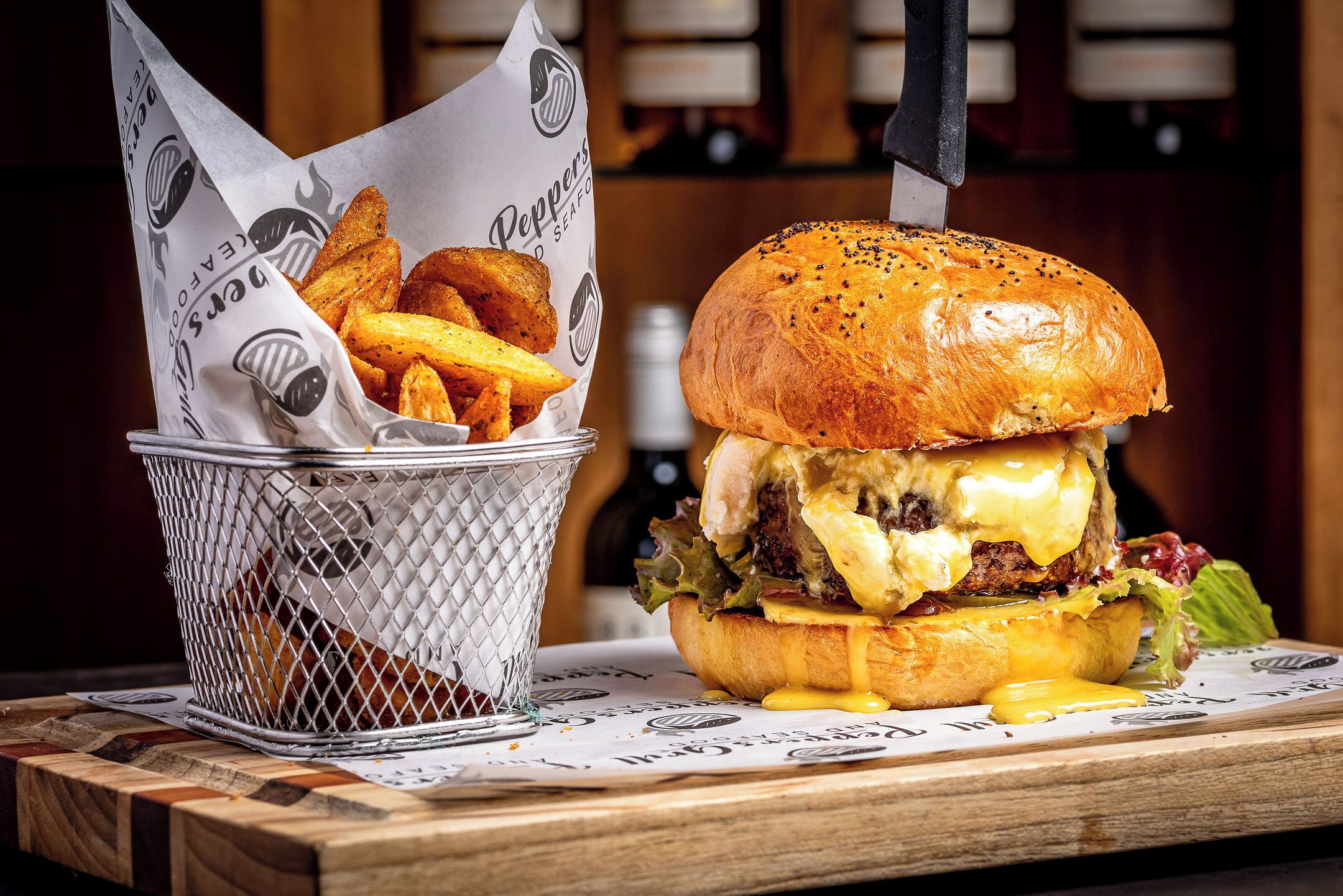 A burger with cheese and a basket of fries on a wooden table.
