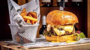 A burger with cheese and a basket of fries on a wooden table.