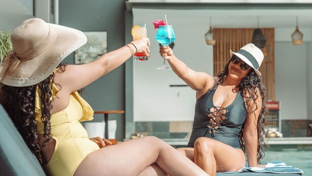 Twee personen zitten bij een zwembad, met drankjes in hun handen.