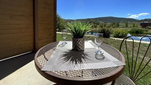 A round metal table with a woven placemat, a potted plant, and two wine glasses on a balcony overlooking a scenic landscape with hills and a lake. - Relax, Adventure, Views, Amenities +Memories (King) (Granby)