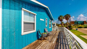 Une maison bleue avec une terrasse en bois, une balustrade blanche et une pancarte sur laquelle on peut lire « MAISON DE PLAGE ».