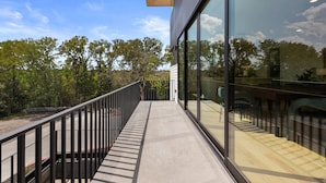 Ein modernes Gebäude mit großen Glasfenstern, einer Holzterrasse und Blick auf Bäume.