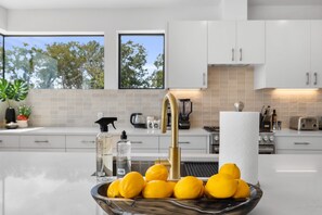 A modern kitchen with white cabinets, a stainless steel sink, and a bowl of lemons on the counter.