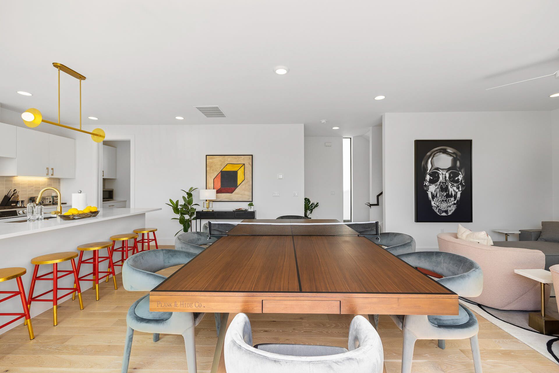 Un espace repas moderne avec une table en bois, des chaises rouges et dorées, et un grand tableau accroché au mur.