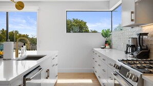 Eine moderne Küche mit weißen Schränken, einem großen Fenster und Blick auf Bäume.