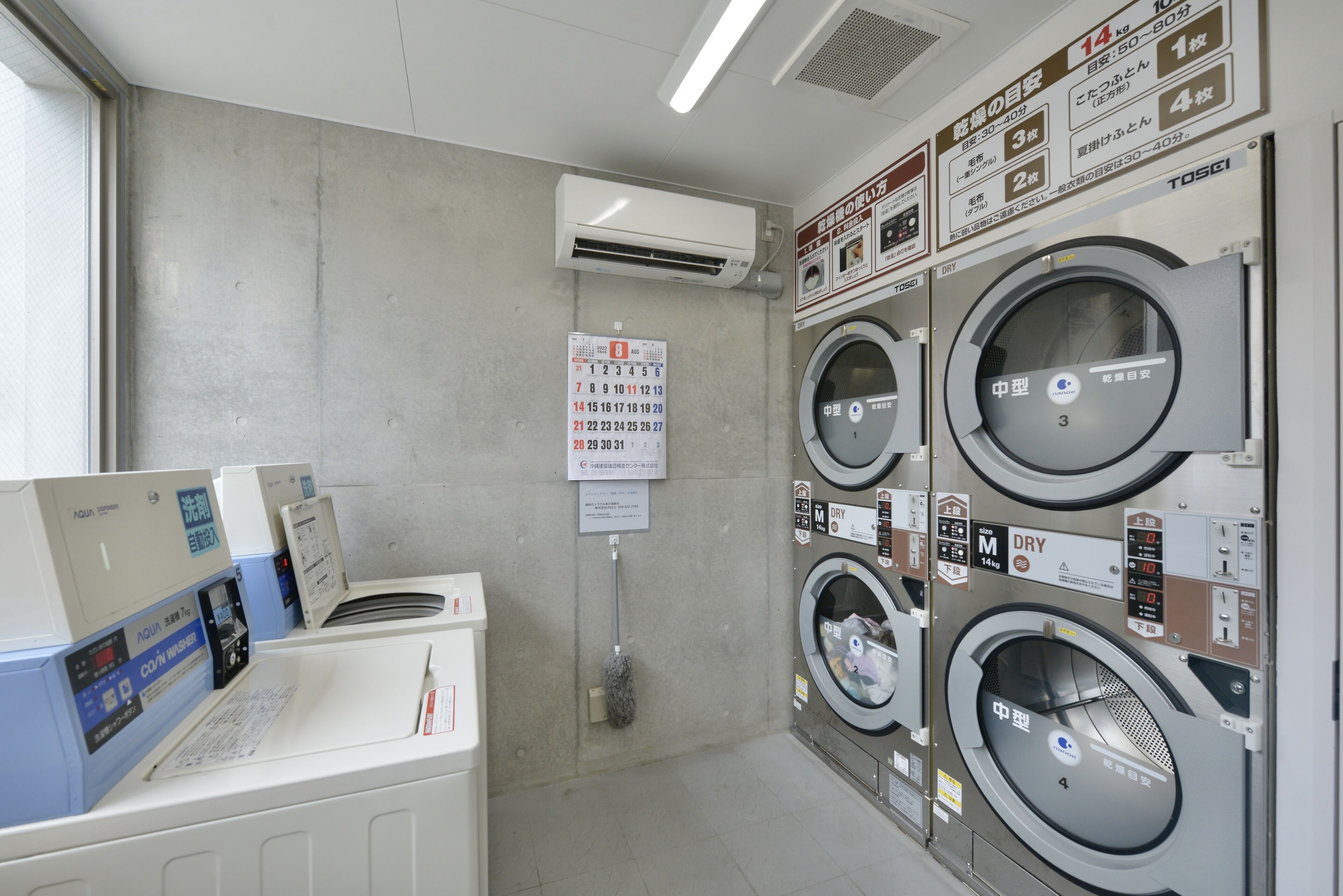 A laundry facility with multiple washing machines, a drying machine, and a calendar on the wall.
