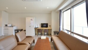Ein Hotelzimmer mit einer Couch, einem Holztisch, einem Fernseher, einer kleinen Küchenzeile und einem großen Fenster.