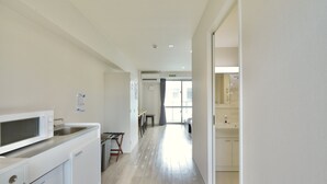 Eine moderne Küche mit Mikrowelle, Spüle und Schränken. Ein Essbereich mit Tisch und Stühlen ist ebenfalls vorhanden. Der Raum verfügt über ein großes Fenster und eine Tür zu einem weiteren Zimmer.