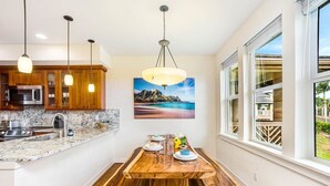 A modern kitchen with wooden cabinets, a marble countertop, and a dining table with benches. There is a large window with a view of the outdoors.
