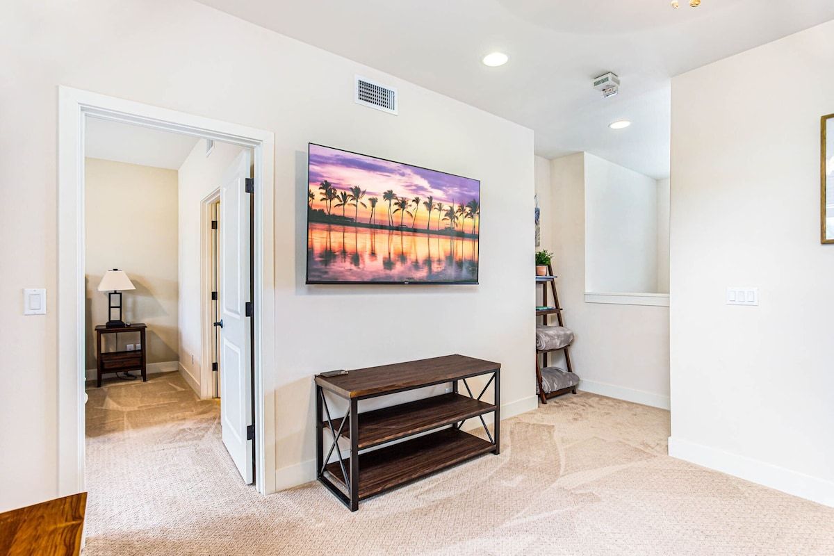 A hallway with a painting of a sunset over water, a dark wooden console table, and a lamp in the background.