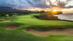 A golf course with bunkers and a view of the ocean at sunset.
