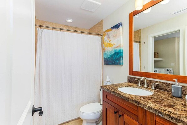 A bathroom with a shower curtain, a toilet, a sink with a marble countertop, and a mirror.