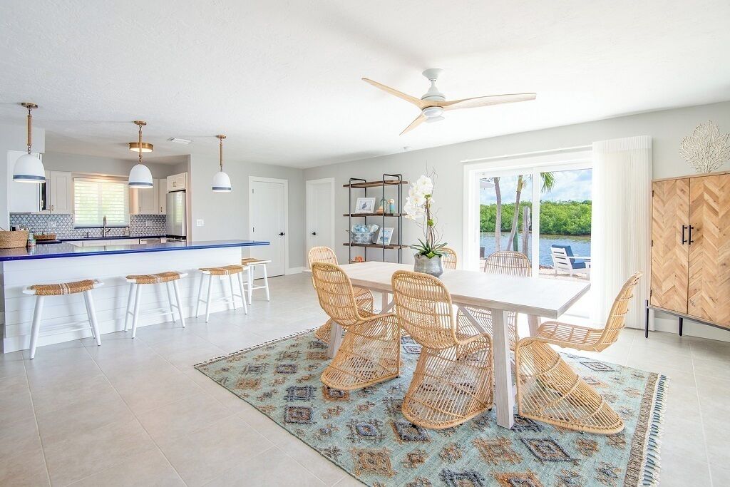 A spacious kitchen with a central island, white bar stools, and a dining area with wicker chairs.