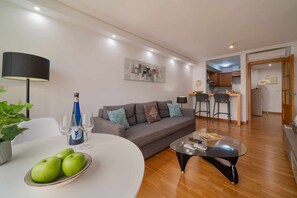 Uma sala de estar moderna com um sofá cinzento, uma mesa de centro de vidro e uma mesa de jantar com um prato de maçãs verdes.