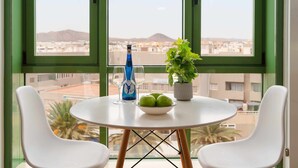 Une table ronde avec deux chaises blanches, une bouteille, un verre et un bol de pommes vertes.