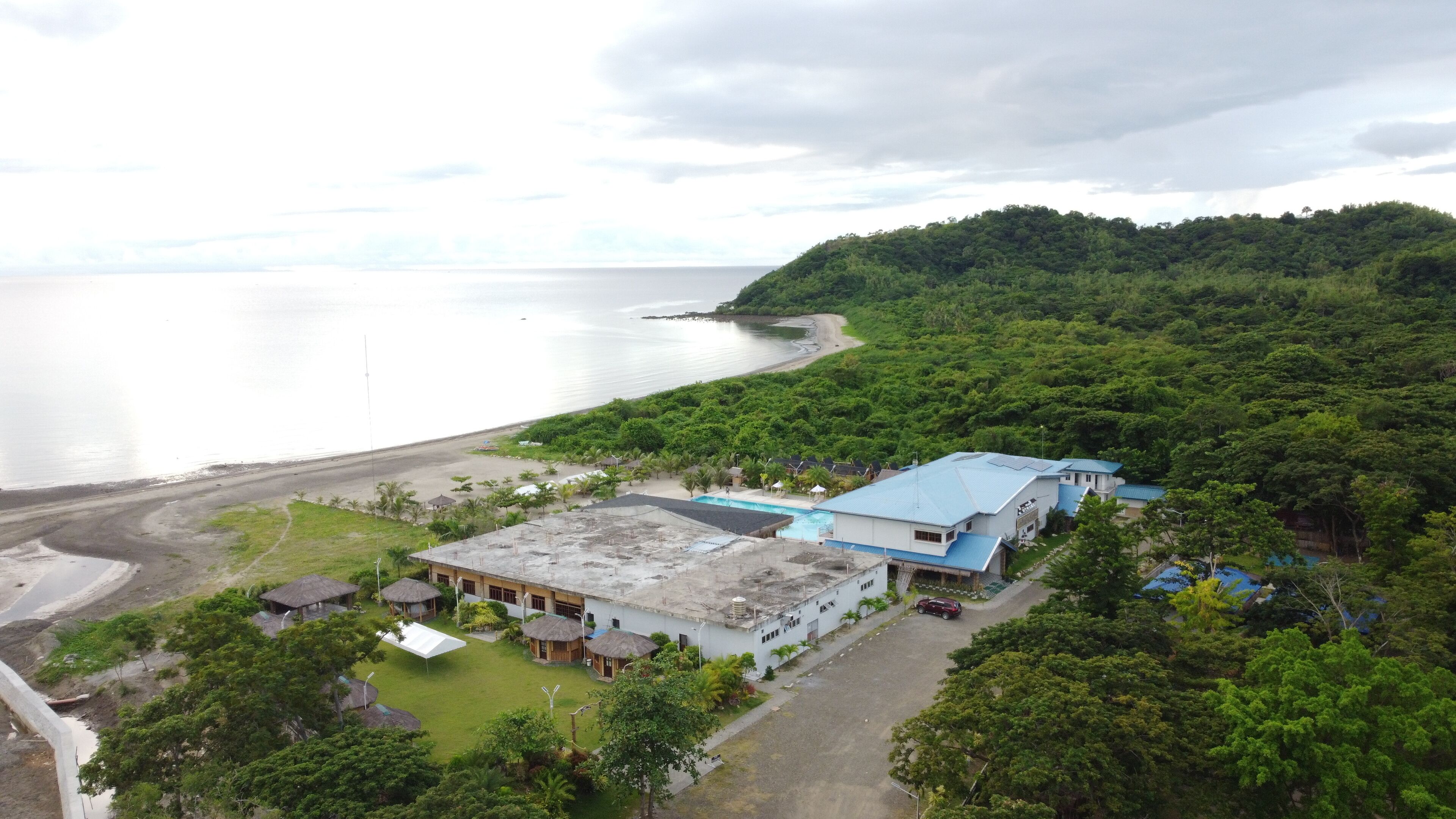A coastal hotel with a large building, a swimming pool, and a beach.