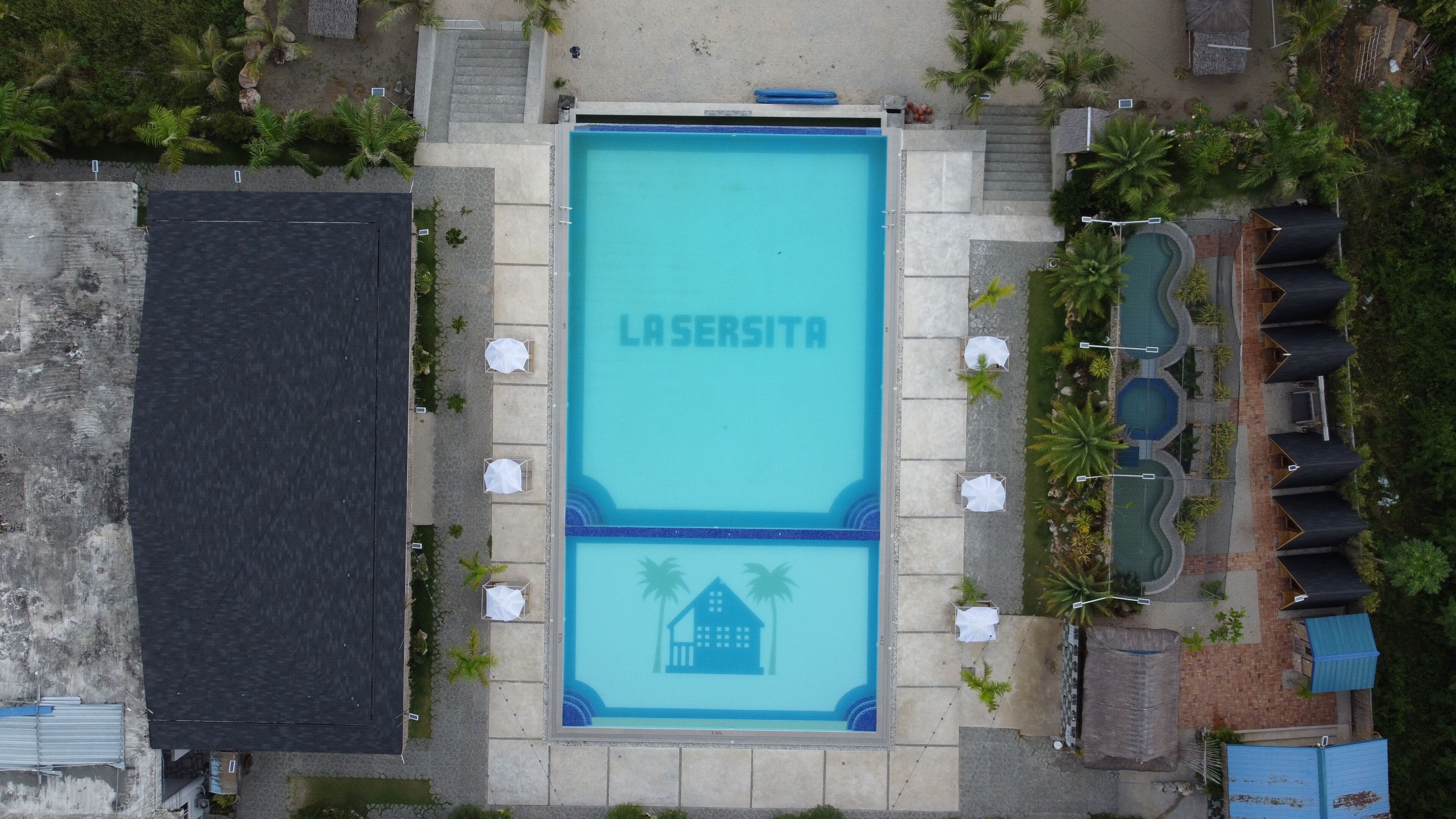An aerial view of a swimming pool area with the name 'LASERSITA' and a house icon, surrounded by lounge chairs and palm trees.