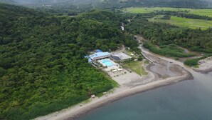 Vue aérienne d’un complexe hôtelier doté d’une piscine, d’une plage et d’une végétation luxuriante.