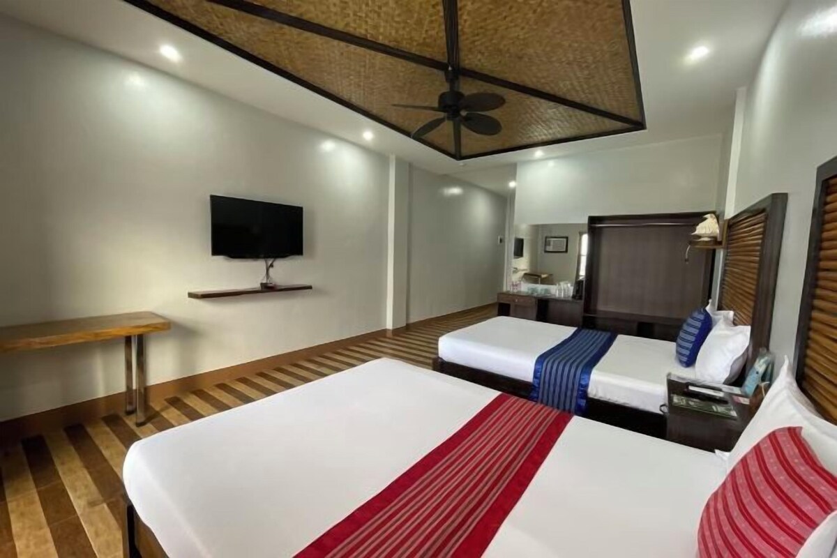 Una habitación de hotel con una cama grande, un escritorio, un televisor y un ventilador de techo.