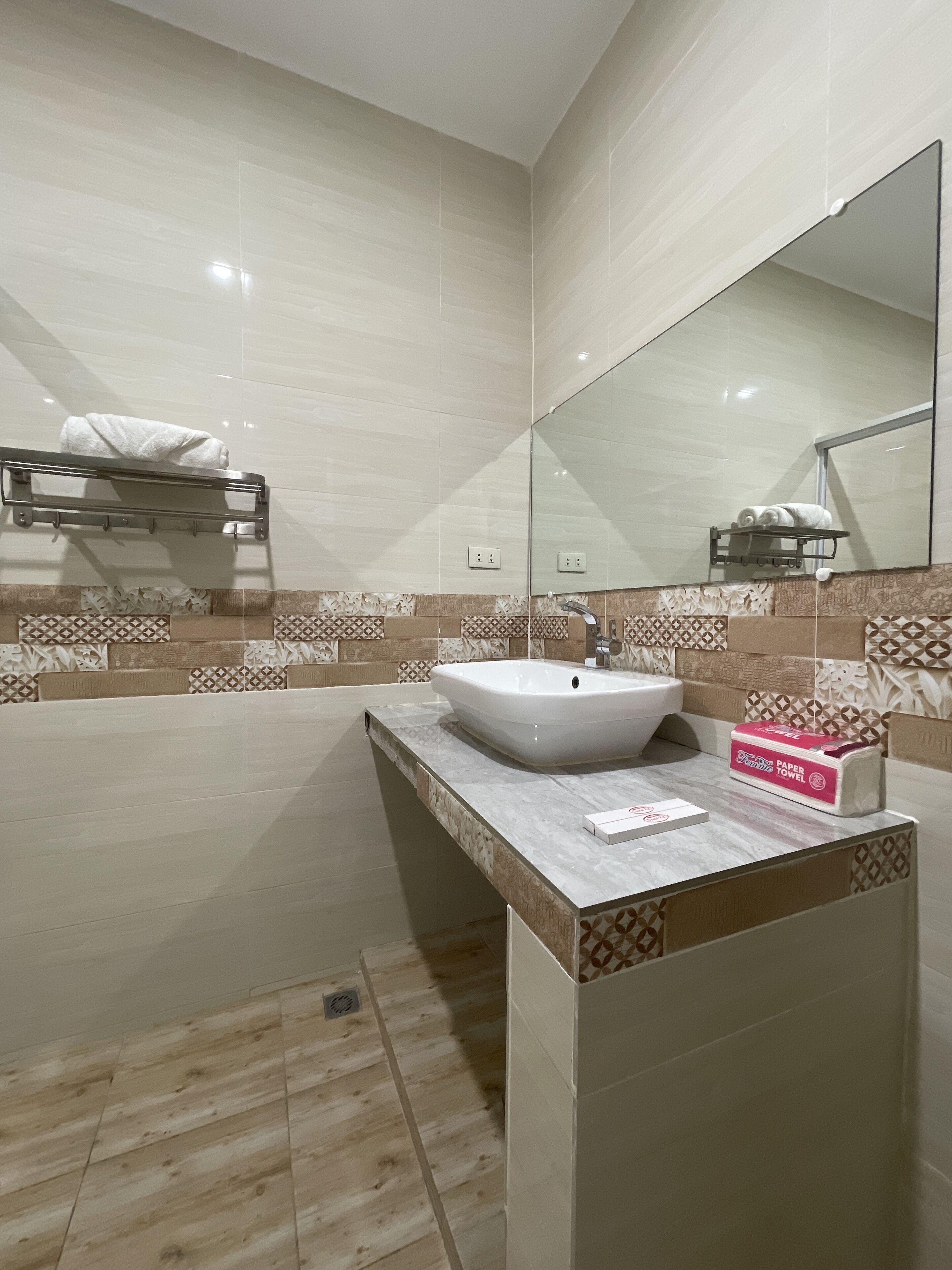 A modern bathroom with a large mirror, a white sink, and a towel rack.