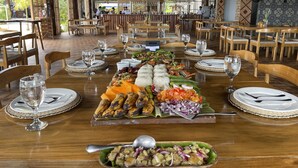 Un restaurant avec des tables et des chaises en bois, un buffet proposant divers plats et une vue sur l’extérieur.