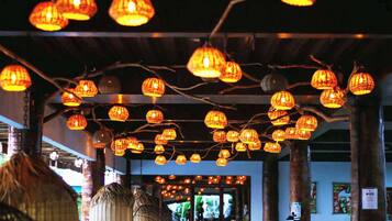 A restaurant interior with hanging lanterns, wooden beams, and a view of the street outside.