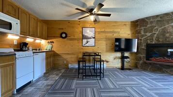 A kitchen with wooden cabinets, a microwave, a stove, a coffee maker, a clock, a television, and a stone fireplace.