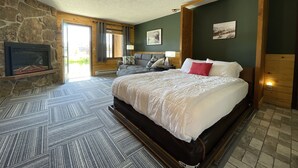 Ein Schlafzimmer mit Kamin aus Stein, einem großen Bett, einem hölzernen Kopfende und Blick ins Freie.