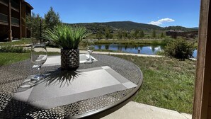 Ein runder Gartentisch mit einem Blumentopf und zwei Weingläsern, mit Blick auf einen See und Gebäude im Hintergrund.
