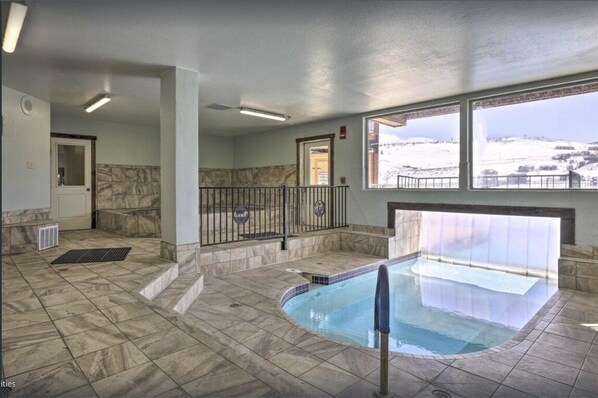 An indoor swimming pool with a view of a snowy landscape through large windows.