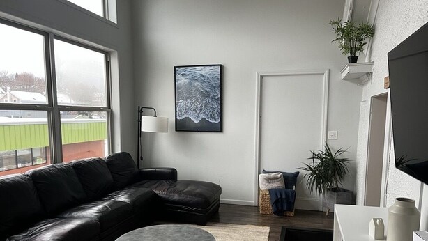 Ett modernt vardagsrum med en svart lädersoffa, ett runt soffbord och ett stort fönster med utsikt över en idrottsplats.
