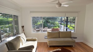 A spacious room with a sofa, a small round table, and a large window offering a view of a garden.