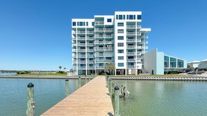 Un hotel frente al mar con un muelle de madera que lleva a una piscina, arquitectura moderna y cielo despejado.