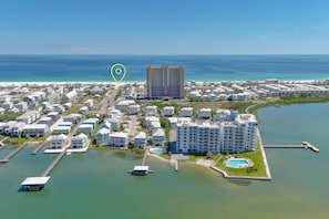 An aerial view of a coastal residential area with multiple buildings, a marina, and a large hotel with a pool.