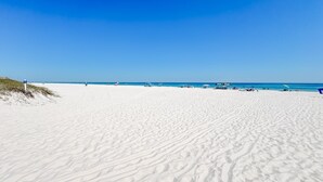 Una playa de arena blanca, cielo azul despejado y algunas sillas y sombrillas de playa.