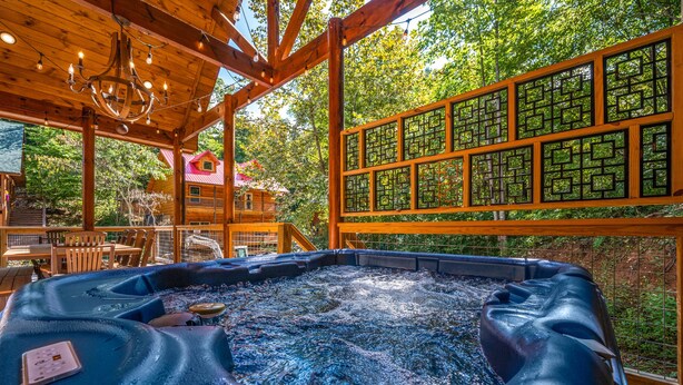 Une cabane en bois dotée d’un bain à remous, d’une terrasse en bois et offrant une vue sur une autre cabane dont le toit est rouge, visible au loin.