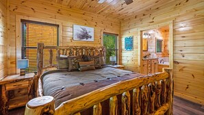 Une chambre située dans un chalet en rondins, avec un lit en bois, un ventilateur de plafond et une fenêtre équipée de stores.
