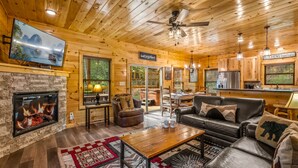 Un intérieur de chalet chaleureux avec une cheminée, des meubles en cuir, un téléviseur et un coin cuisine.