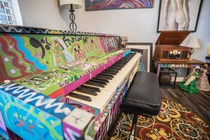 A piano with colorful graffiti art, a black bench, and a patterned rug in a room with a lamp and a music player.