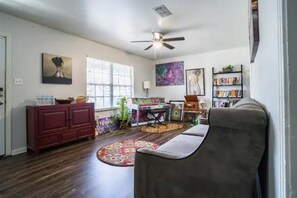 A living room with a ceiling fan, a red cabinet, a gray sofa, a colorful rug, and a bookshelf.