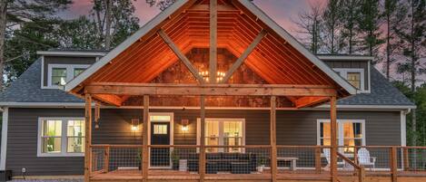 A two-story house with a wooden deck, a covered porch, and a large window overlooking the deck.