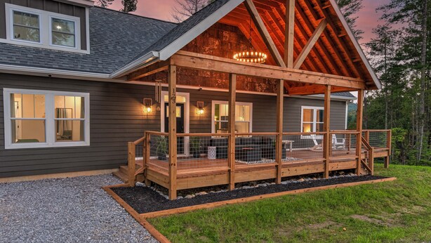 Een tweelaags huis met een houten terras, een overdekte veranda en een groot raam op de bovenverdieping.