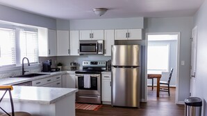 Uma cozinha moderna com armários brancos, eletrodomésticos de aço inoxidável, bancada de mármore e vista para a área de jantar.
