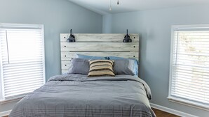 Quarto com cama cinza, cabeceira de madeira e duas luminárias de cabeceira.